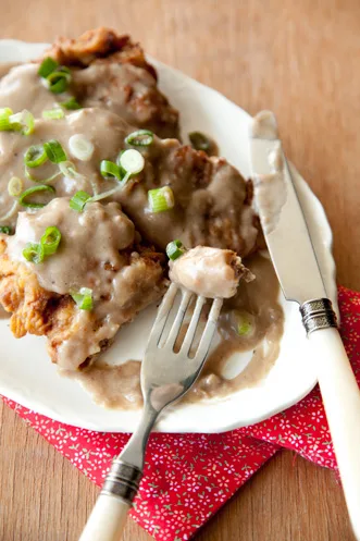 Paula Deen Country-Fried Steak smothered in brown pan gravy with onions on a plate