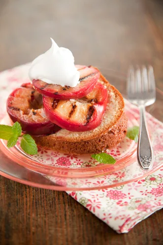 Sliced cream cheese pound cake topped with grilled plums and honey on a serving plate