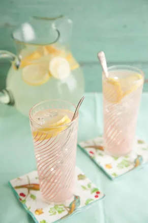A tall glass of Paula Deen Lemonade with a lemon slice and sprig of mint on a sunny table