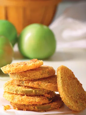 Oven-fried green tomatoes coated in cornmeal on a baking sheet