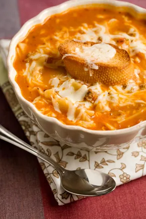 A bowl of Paula Deen Tastes Like Lasagna Soup topped with bubbly broiled mozzarella and a garlic crostini slice