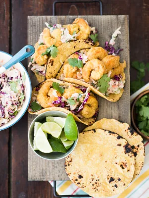Paula Deen adobo shrimp tacos with smoked BBQ chipotle coleslaw on a wooden board with lime wedges and tortillas