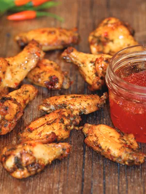 Paula Deen air fryer crispy red-pepper-jelly wings glazed and herb-flecked on a wooden board beside a jar of red pepper jelly