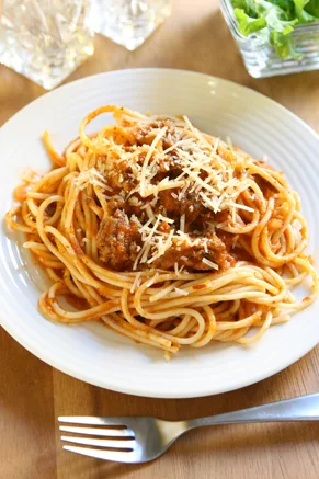 Paula Deen Alice Jo's spaghetti sauce spooned over spaghetti on a white plate topped with grated Parmesan