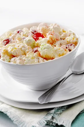 Paula Deen ambrosia salad in a white bowl with marshmallows, pineapple, oranges and maraschino cherries in a creamy dressing