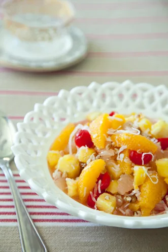 Paula Deen ambrosia in a white lattice bowl with orange sections, pineapple chunks, maraschino cherries and shredded coconut