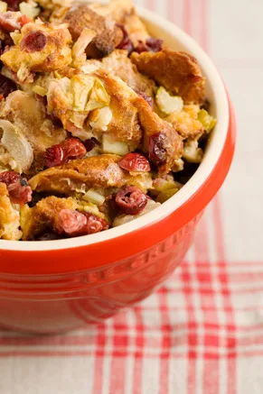 Paula Deen apple cranberry stuffing in a red baking bowl with golden bread cubes, chopped apples, celery and dried cranberries