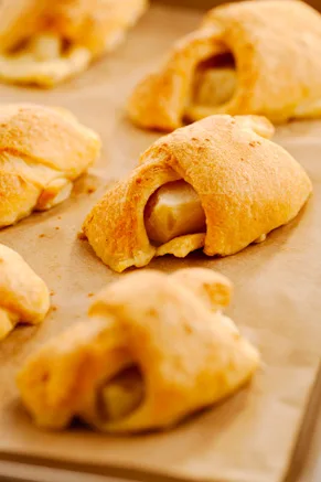Paula Deen apple dumplings made with apple wedges wrapped in golden baked crescent rolls on a parchment-lined pan