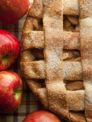Paula Deen apple pie recipe with a sugared lattice crust beside fresh red apples on a plaid cloth