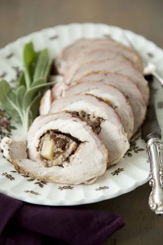Sliced Paula Deen apple stuffed pork loin showing apple and cornbread stuffing spiral on a floral platter with fresh sage