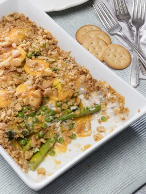 Paula Deen asparagus and pea casserole in a white baking dish topped with crushed buttery crackers, cheddar, peas and sliced eggs