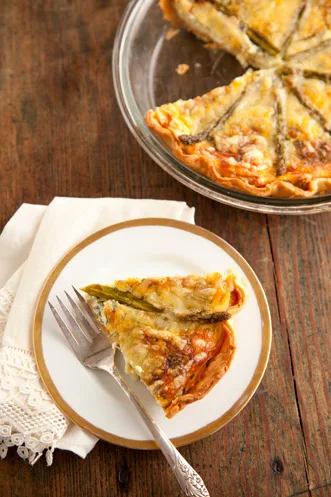 Paula Deen asparagus quiche in a glass pie plate with one golden slice on a gold-rimmed plate beside a fork