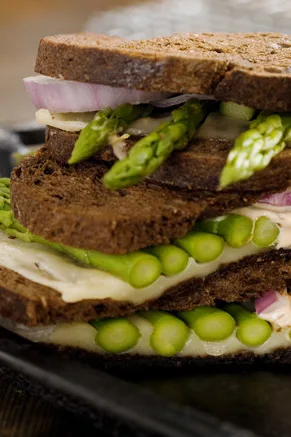 Paula Deen asparagus sandwich stacked on pumpernickel bread with asparagus spears, melted Jack cheese and red onion rings