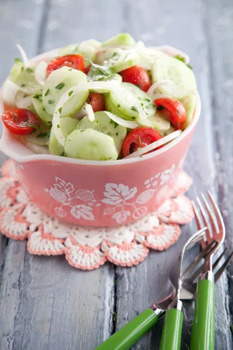 Paula Deen Aunt Peggy's cucumber, onion, and tomato salad in a pink vintage bowl with sliced cucumbers, cherry tomatoes and white onion