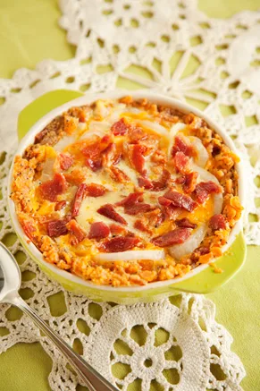 Paula Deen bacon onion pie in a green dish topped with melted cheddar, crumbled bacon and a cheese cracker crust