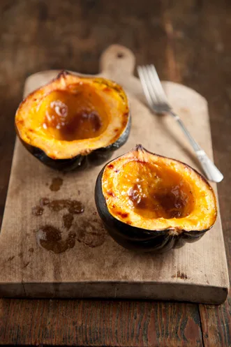 Paula Deen baked acorn squash with brown sugar and butter, two glazed halves on a wooden cutting board with a fork