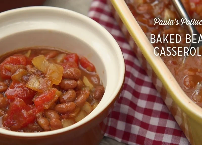Paula Deen baked bean casserole with diced tomatoes and onion served in a small ceramic bowl beside a yellow baking dish