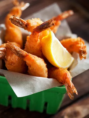 Paula Deen baked coconut shrimp piled in a paper-lined green basket with a lemon wedge