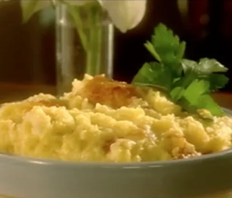 Paula Deen baked garlic cheese grits in a blue-gray dish with a golden cheesy top and a sprig of parsley