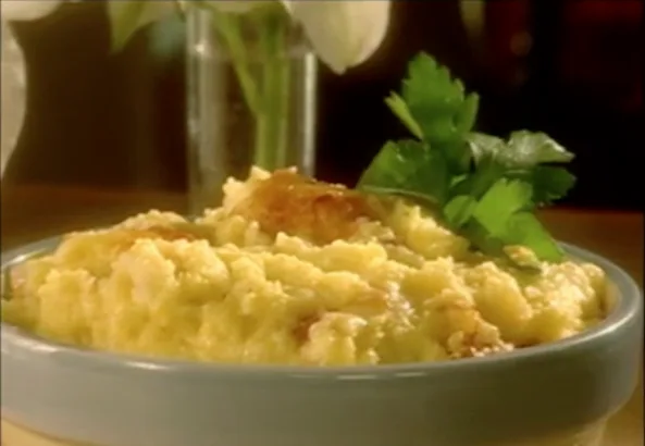 Paula Deen baked garlic cheese grits in a blue-gray dish with a golden cheesy top and a sprig of parsley