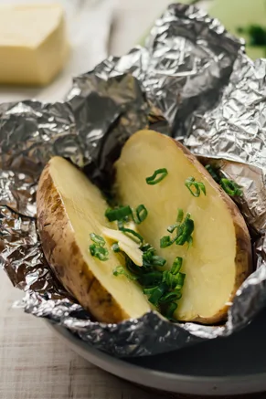 Paula Deen baked grilled potato split open in foil and topped with butter and chopped green onions