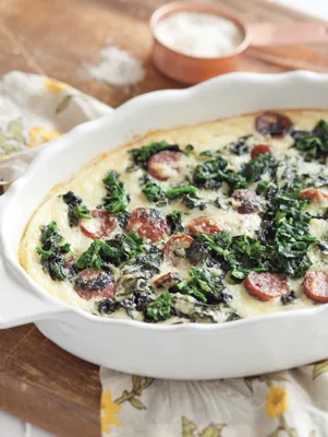 Paula Deen baked grits and greens casserole with sausage slices and wilted kale in a white baking dish