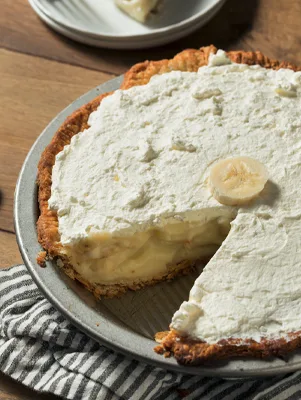 Paula Deen banana cream pie topped with whipped cream and a banana slice, with one slice cut out showing the custard filling
