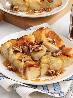 Paula Deen banana pudding bread pudding with banana slices, chopped pecans and maple syrup on a white plate