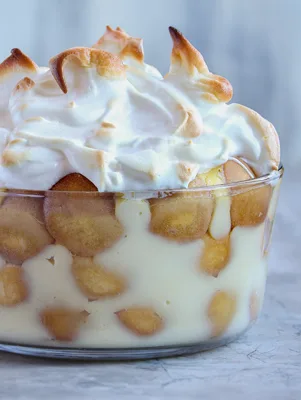 Paula Deen banana pudding with meringue in a glass dish, layered with vanilla custard, banana slices and wafers under golden toasted meringue peaks