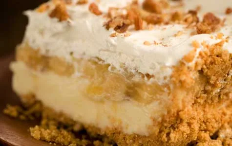 Paula Deen banana split cake with pineapple, showing a graham cracker crust, creamy filling, bananas and whipped topping with nuts