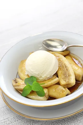 Paula Deen bananas foster with caramelized banana slices in a brown sugar sauce topped with a scoop of vanilla ice cream and a mint sprig