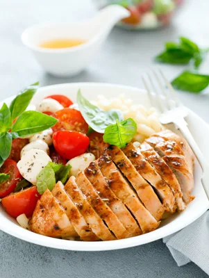 Paula Deen basil grilled chicken sliced on a white plate with cherry tomatoes, fresh mozzarella and basil leaves