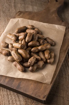 Pile of Paula Deen Becky Polk's boiled peanuts in their shells on brown parchment paper over a wooden cutting board