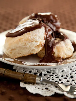 Paula Deen biscuits and chocolate gravy with glossy chocolate sauce poured over split biscuits on a white plate