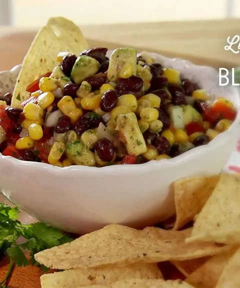 Paula Deen black bean salsa in a white scalloped bowl with a tortilla chip, surrounded by chips and fresh cilantro