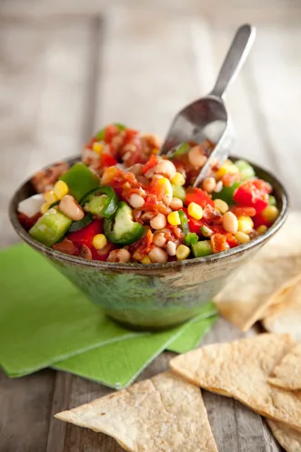 Paula Deen black-eyed pea dip in a rustic bowl with corn, red and green bell peppers and tortilla chips beside it