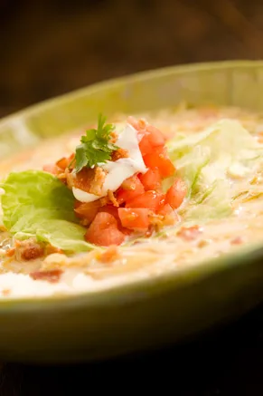 Paula Deen BLT soup in a green bowl topped with diced tomatoes, sour cream, bacon and cilantro over iceberg lettuce