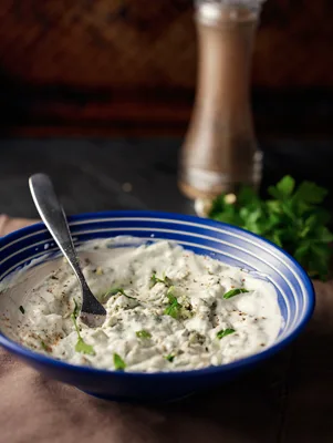 Paula Deen blue cheese dressing in a blue bowl with a spoon, black pepper and fresh herbs on the side