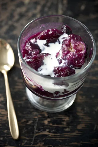 Paula Deen blueberry dumplings in a glass dessert cup with purple berry syrup and a swirl of cream next to a gold spoon