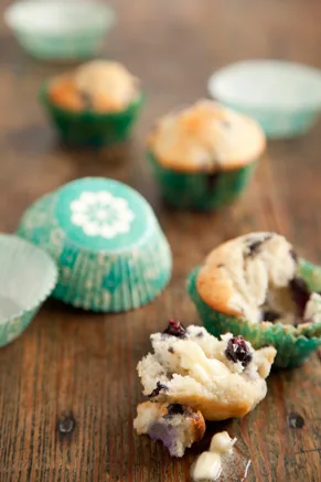 Paula Deen blueberry muffins in green patterned liners on a wooden table with one muffin broken open to show the blueberries