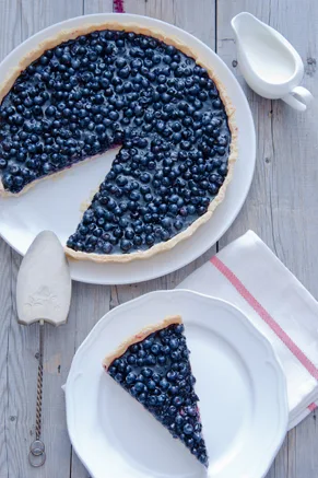Paula Deen blueberry tart with a slice cut out on a white plate, topped with glossy blueberries