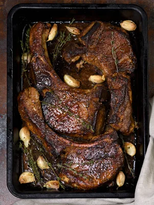 Paula Deen Bobby's seared and baked thick-cut pork chops with garlic cloves and fresh thyme in a dark roasting pan