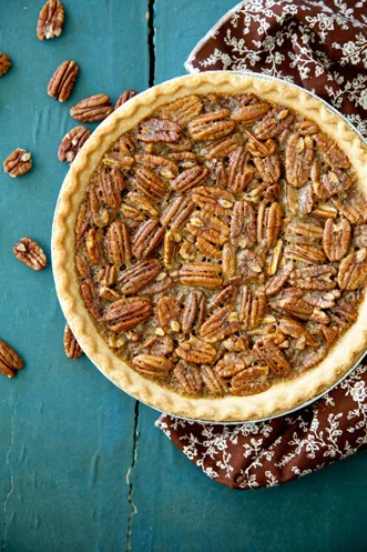 Paula Deen bourbon pecan pie topped with a full layer of pecan halves in a golden crust on a teal wooden table