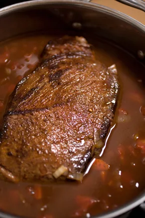 Paula Deen braised beef brisket browned and simmering in a Dutch oven with a red tomato and wine sauce