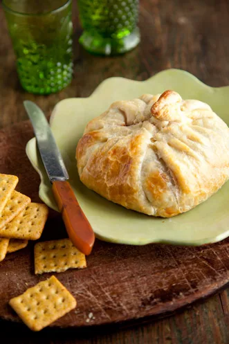 Paula Deen Brie en Croute baked in golden puff pastry on a green plate with crackers and a knife