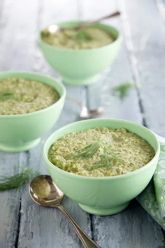 Paula Deen broccoli soup in light green bowls garnished with fresh dill on a weathered blue wooden table