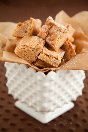 Paula Deen brown sugar chewies cut into squares and dusted with confectioners' sugar in a white hobnail dish lined with parchment