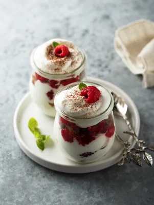 Paula Deen brownie raspberry trifle in two small glass jars topped with whipped cream, a fresh raspberry, mint and cocoa dusting