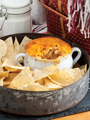 Paula Deen buffalo chicken dip baked golden in a white crock surrounded by tortilla chips in a rustic metal tray