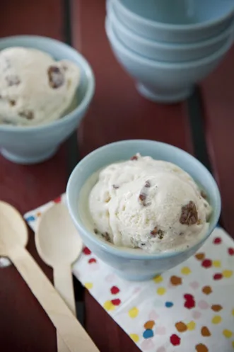 Paula Deen butter pecan ice cream scooped into light blue bowls with toasted pecan pieces, next to wooden spoons on a polka dot napkin